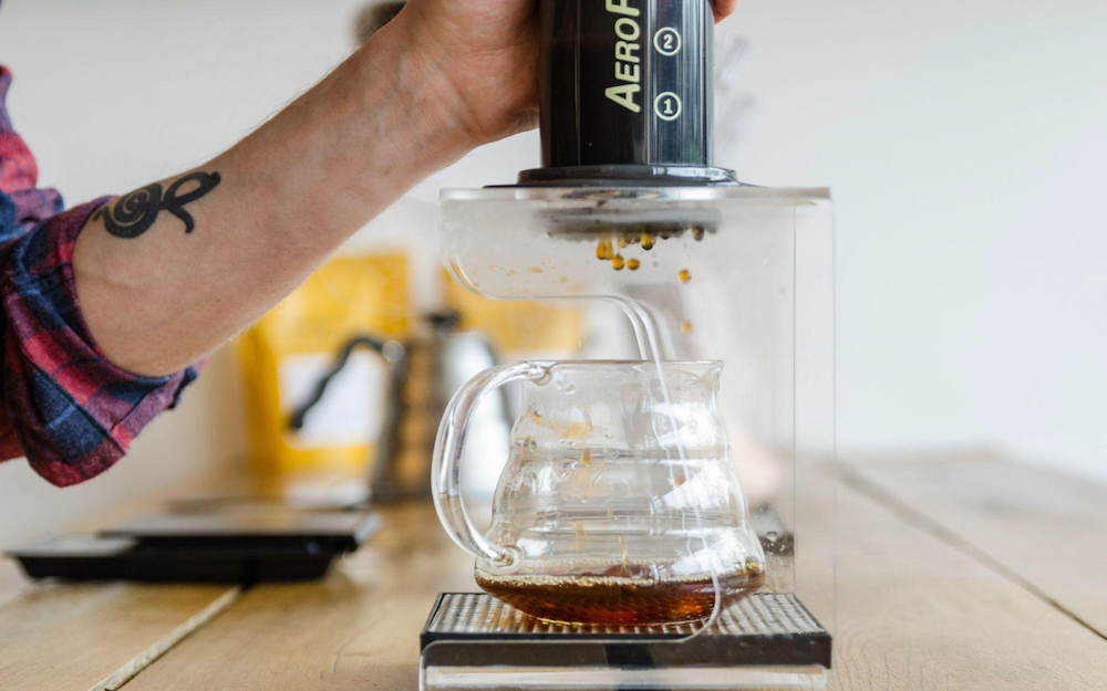 Barista brewing coffee in an AeroPress over a glass carafe.