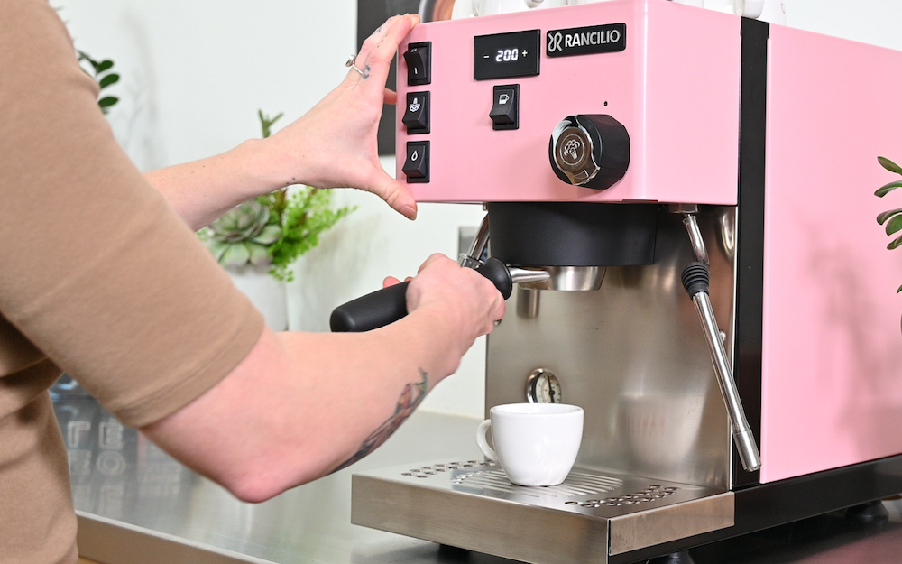 Barista preparing temperature controlled espresso using a pink Rancilio Silvia Pro X espresso machine.
