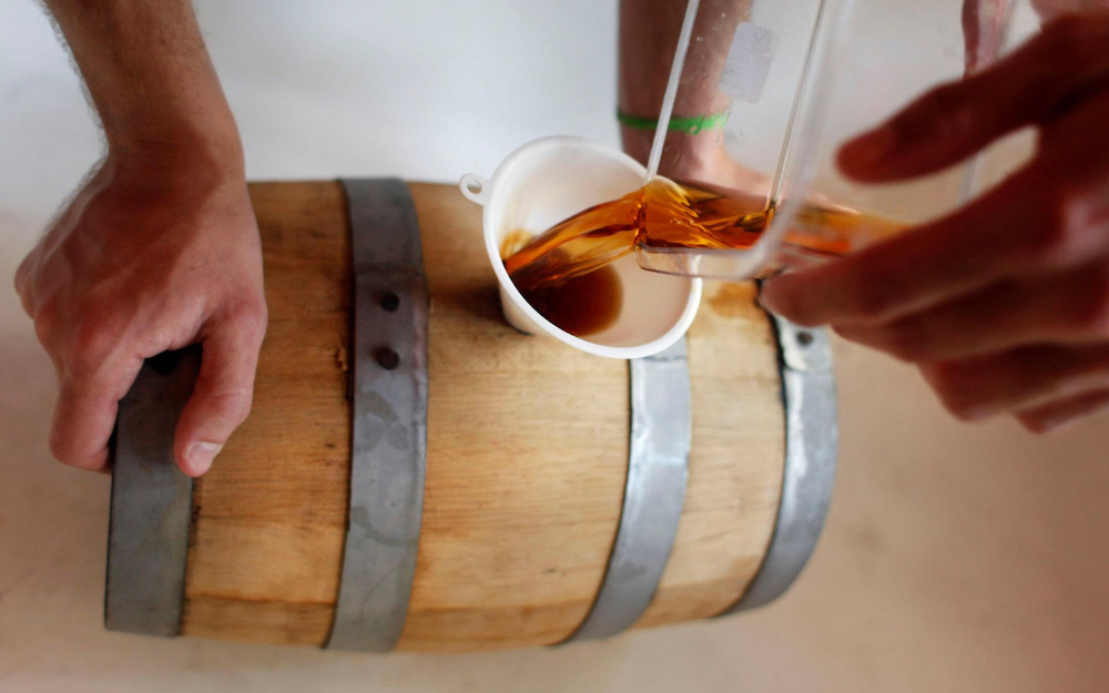 A person pours cold brew into a whiskey barrel.