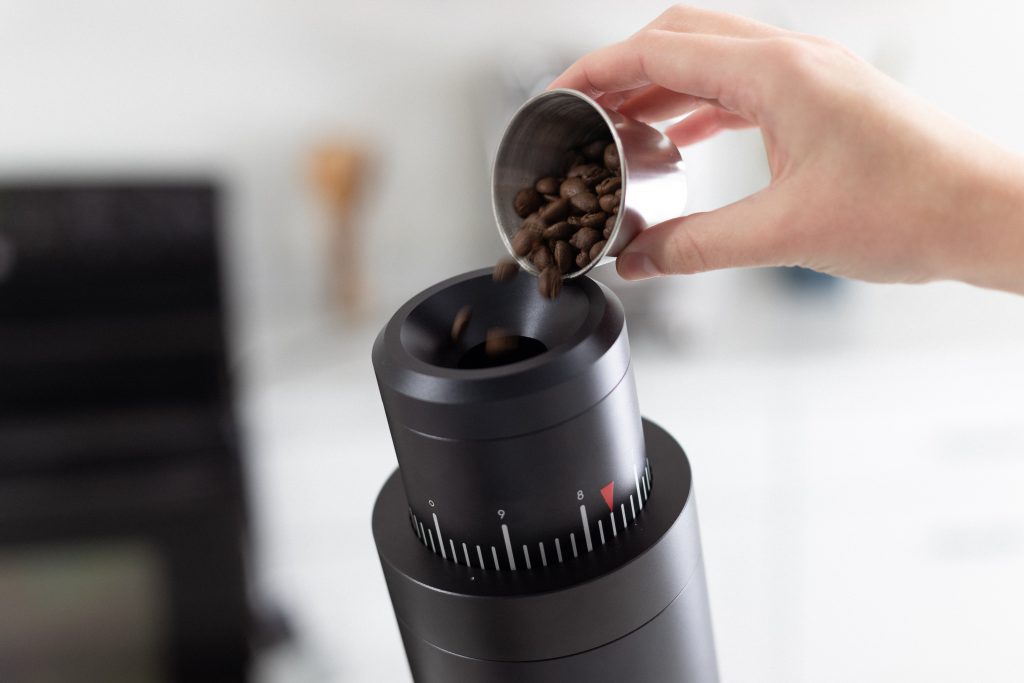 A barista pours coffee beans into a single-dose grinder hopper