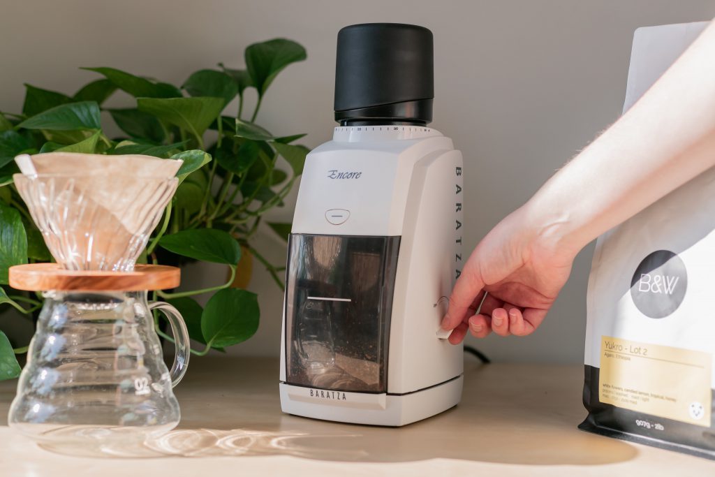A home brewer turns on a white Baratza Encore grinder to grind coffee beans