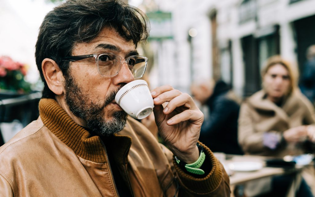 A man sips espresso outside a coffee shop.