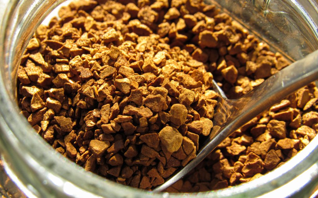 A teaspoon inside a jar of freeze-dried instant coffee.