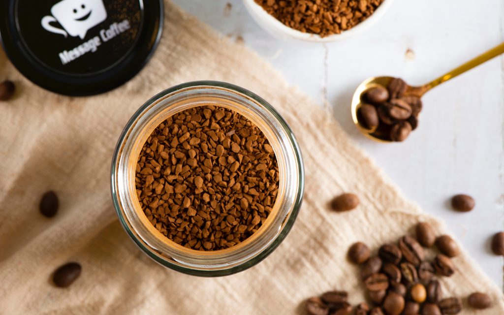 A jar of soluble coffee next to some whole coffee beans.
