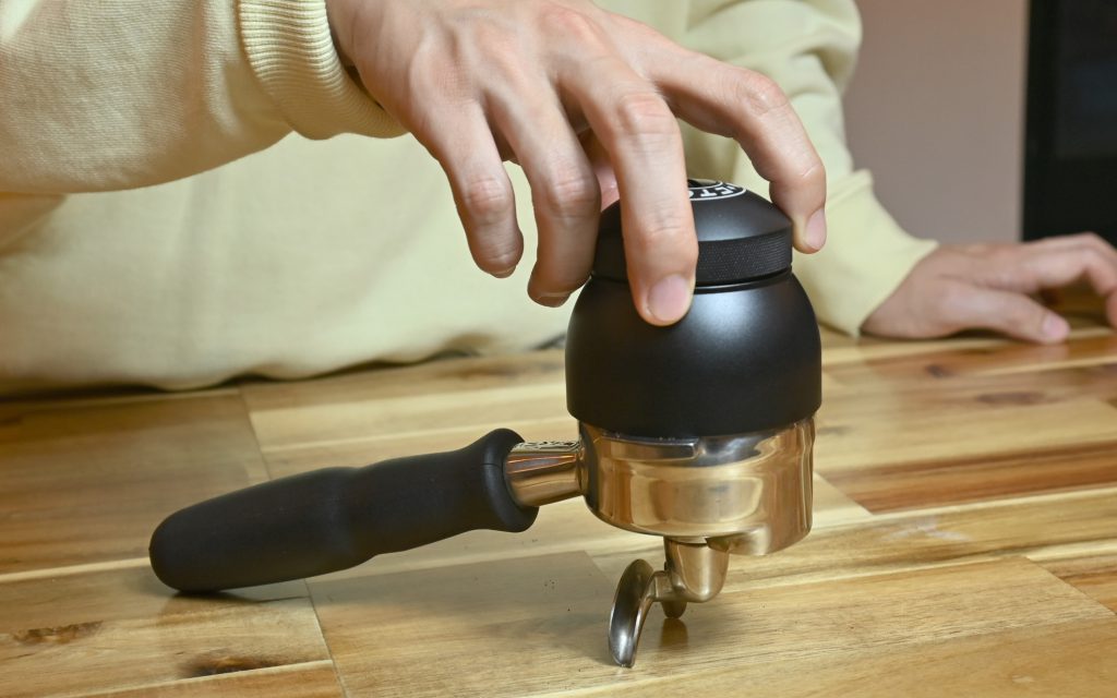A barista uses a Weiss distribution technique tool to ensure even distribution of coffee grounds for espresso.