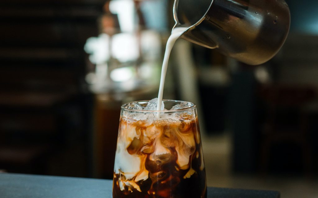 A barista pours milk into a cold coffee drink.