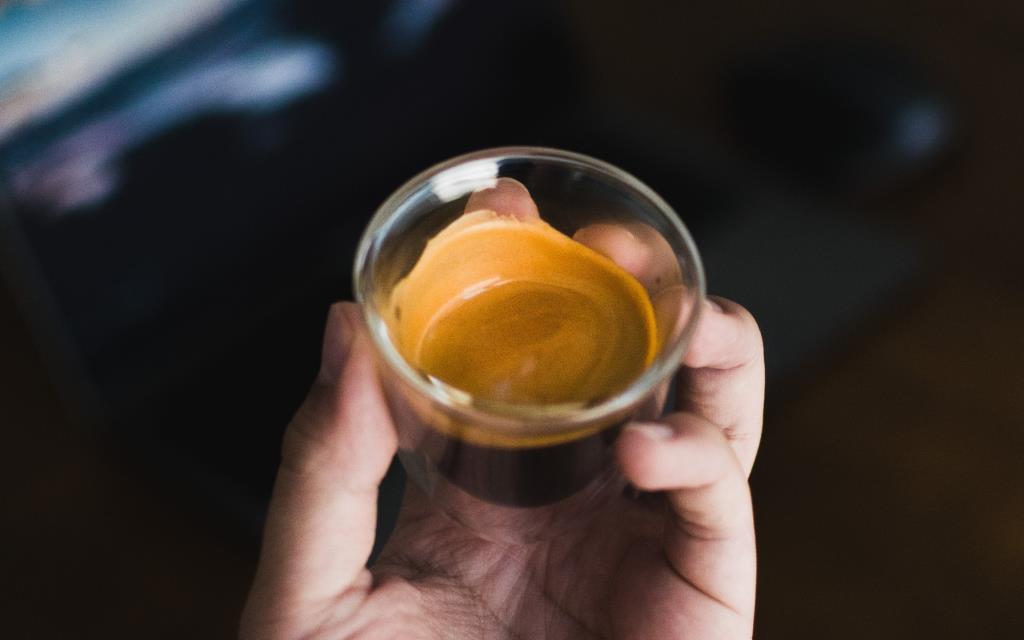 A barista holds a shot of espresso in a glass.