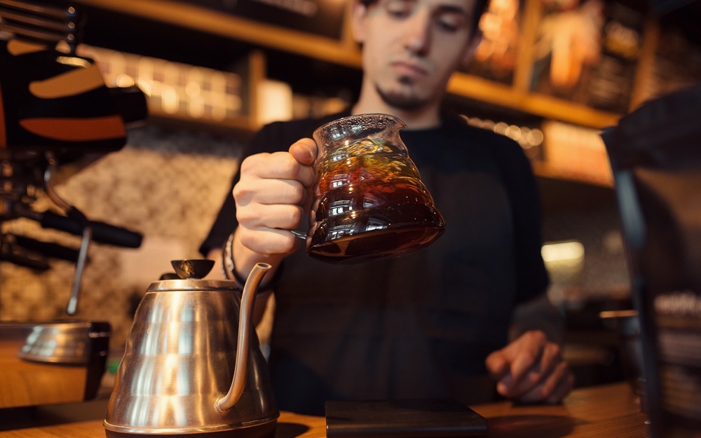 A barista swirls filter coffee in a glass carafe.