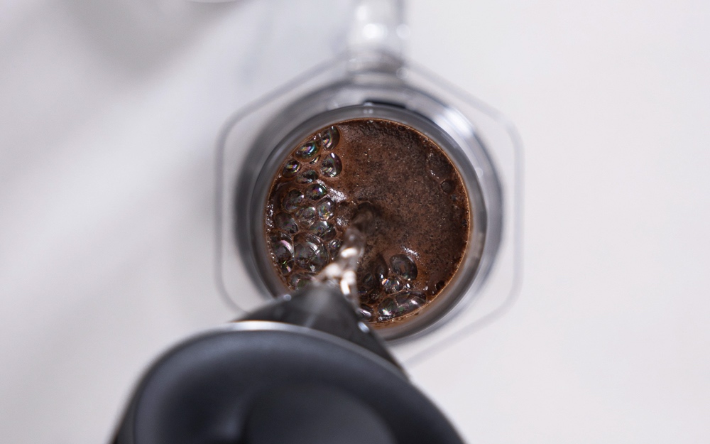 A barista pours hot water into a clear AeroPress.