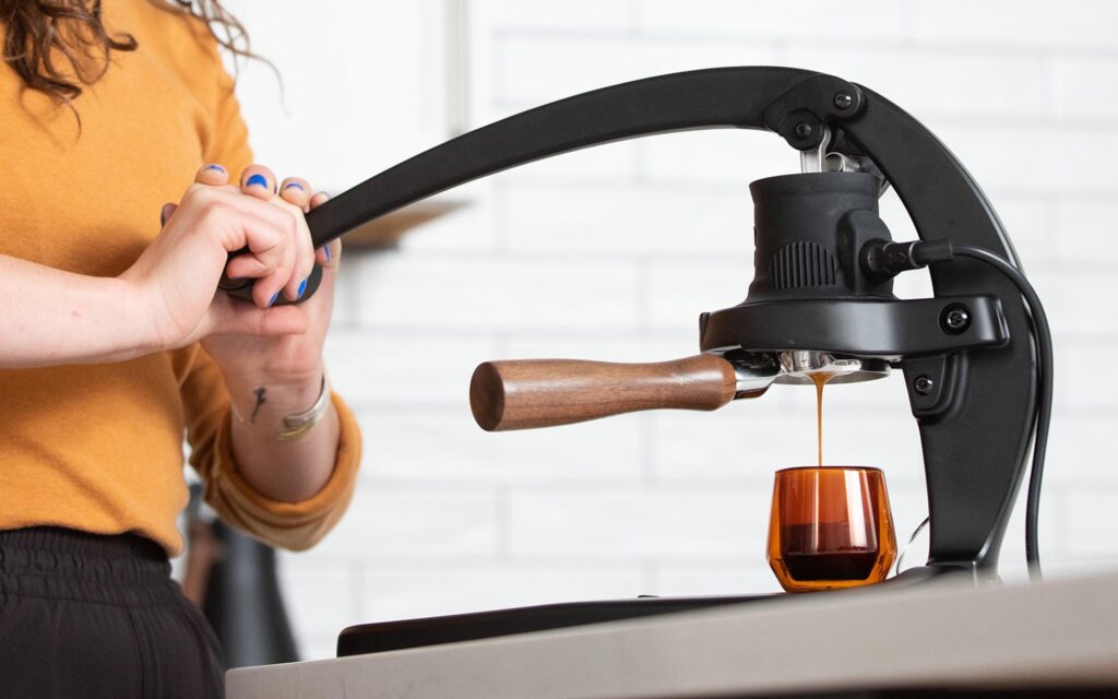 A woman uses a manual espresso machine with a lever.