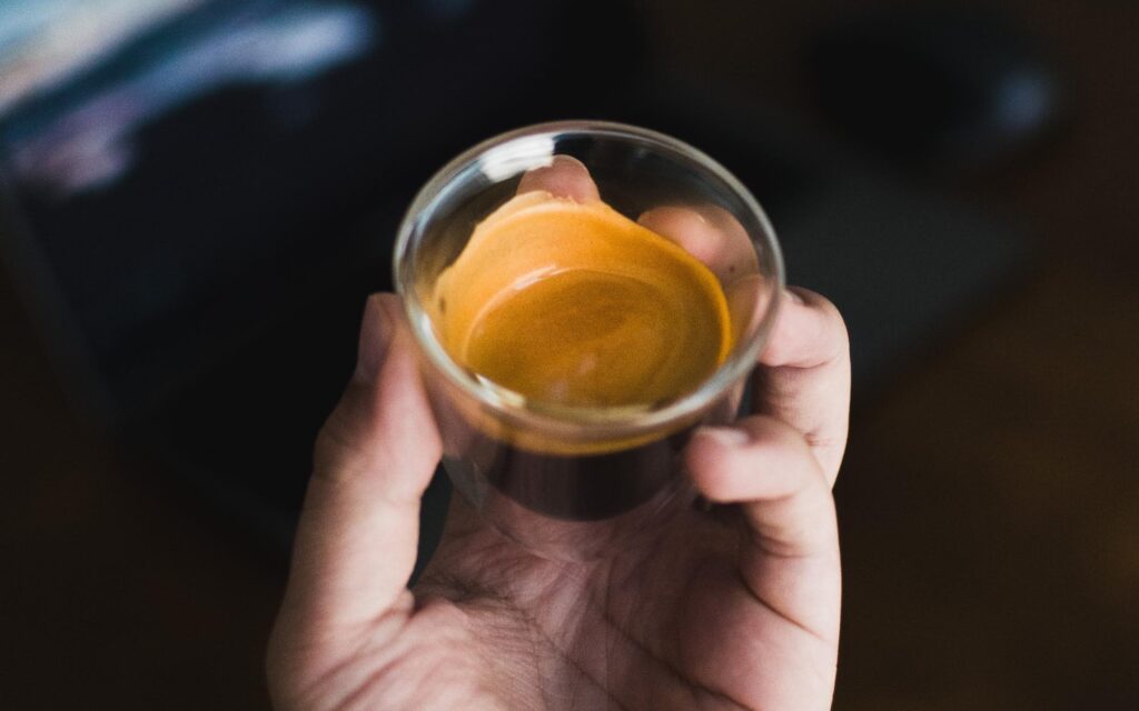 A person holds a single shot of espresso coffee.
