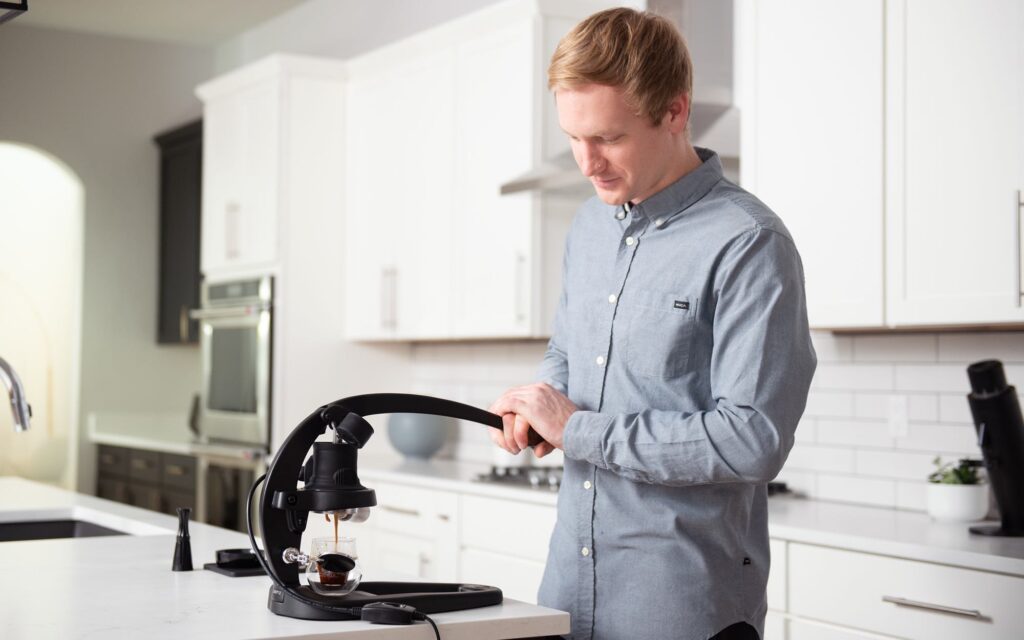 A man uses a manual espresso machine in his kitchen.
