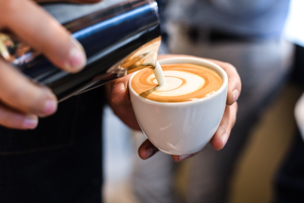 A barista pours a heart latte art design.