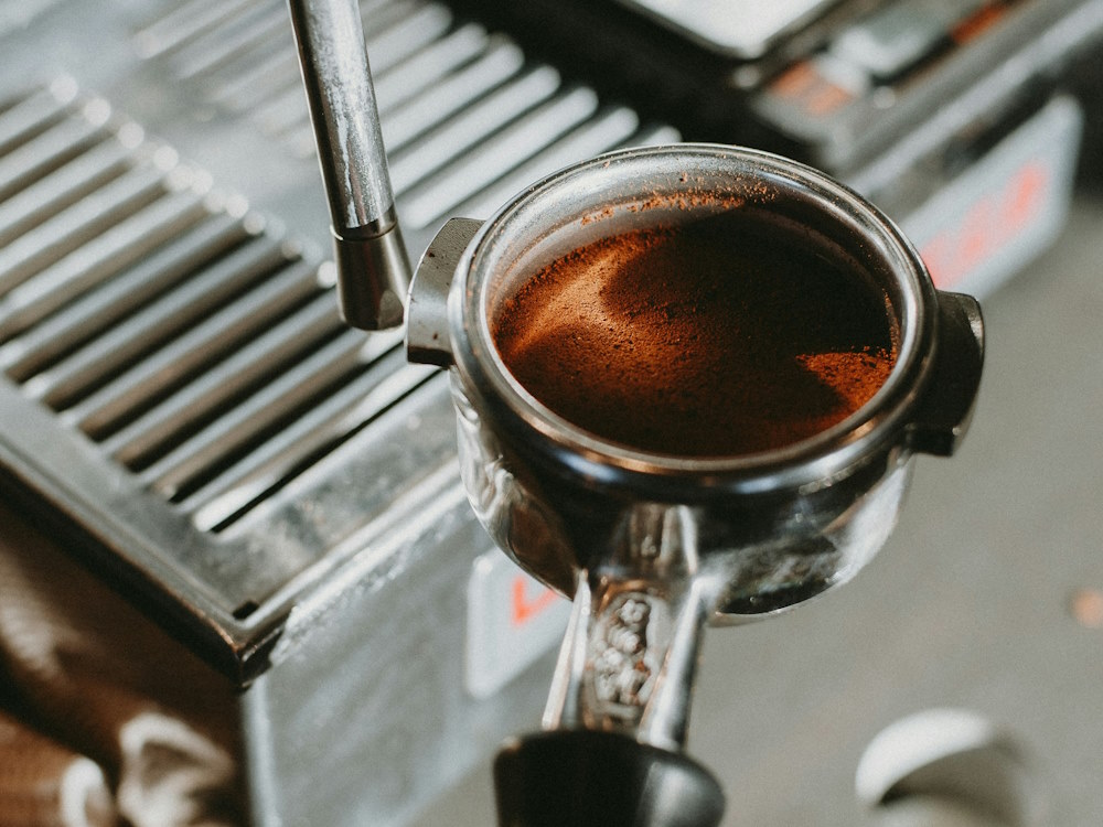 A barista holds a portafilter with a tamped puck before extraction.