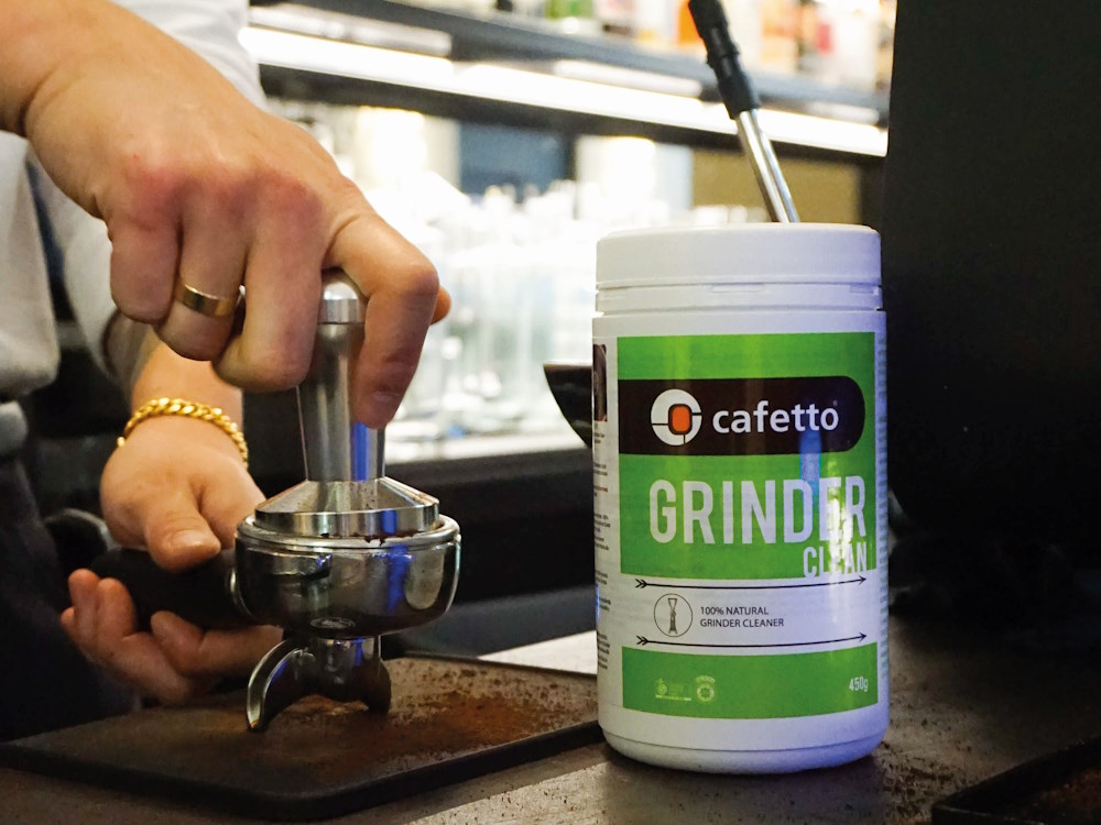A barista tamps coffee next to Cafetto's grinder product to clean equipment.