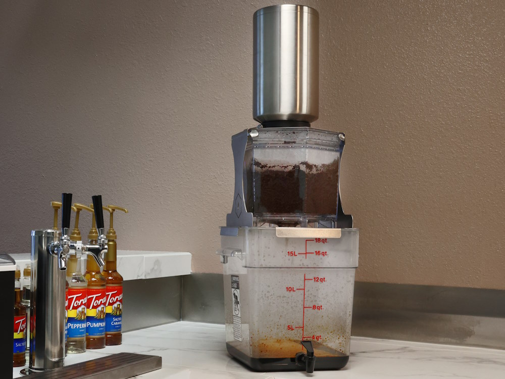 The Hive Café cold brew system next to some syrups in a coffee shop.